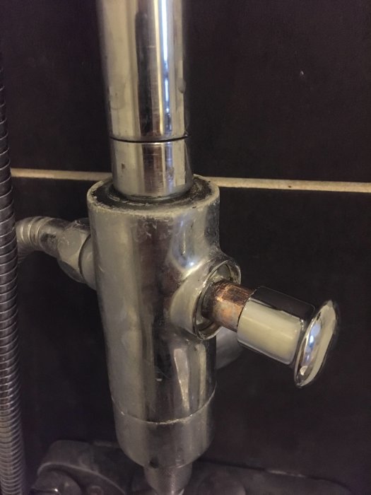 En duschomkastare och dess anslutningar till takdusch och handdusch synlig på en kaklad vägg.