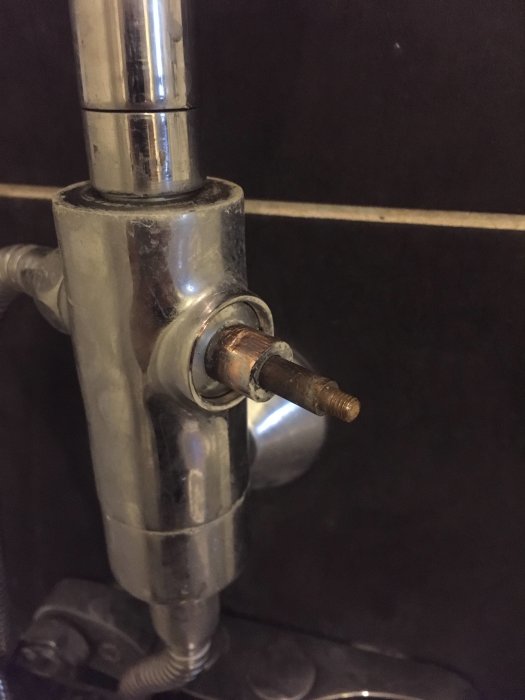 Närbild på en duschomkastare med synlig slitage och möjlig läckage, installerad på kakelvägg.