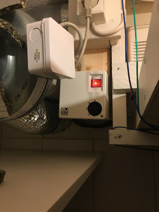 Kanalfläkt installerad i källare med synliga kablar och ventilationsrör.
