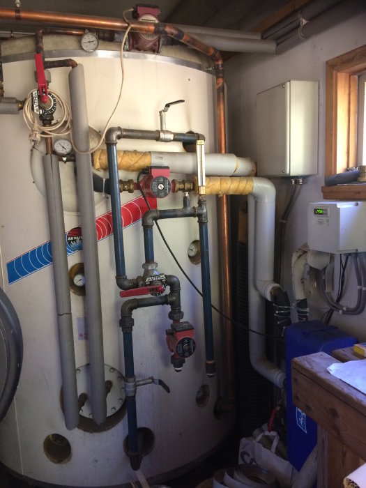 Värmesystem med stor tank, rör och cirkulationspumpar i ett garage.