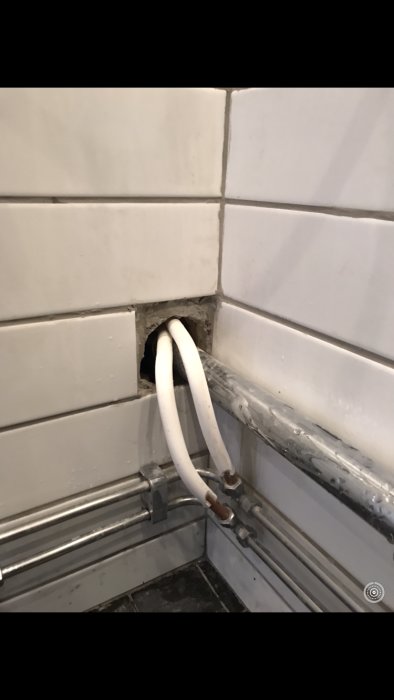 Öppning i väggen med rör och kablar som behöver tätas i ett badrum.