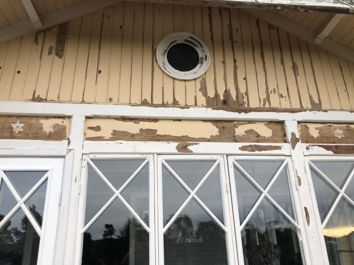 Gamla målade vita stjärnor på trävägg av ett gult hus med skrapad färg och fönster.