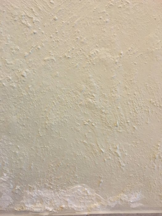 Närbild av en vägg målad med borstat kalkfärg och synlig lagning längst ner.