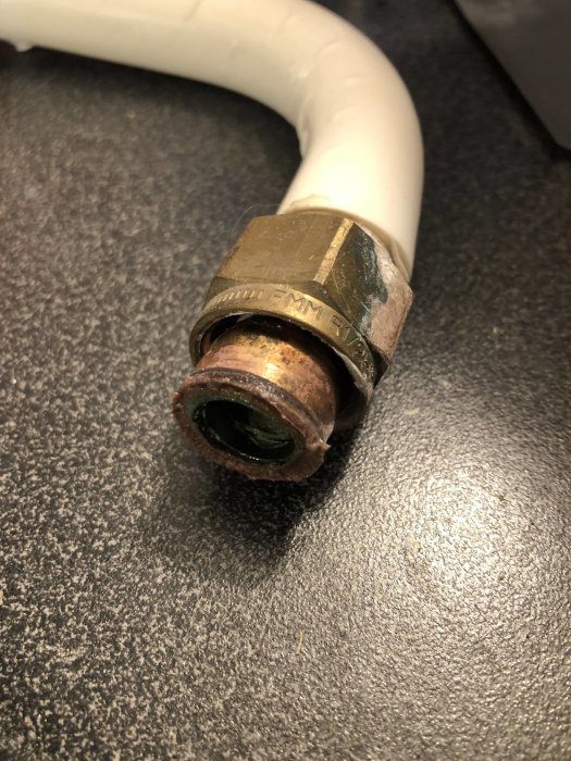 Vit plaströrskoppling med ovanlig och plan ändring, sammankopplad med en metallmutter.