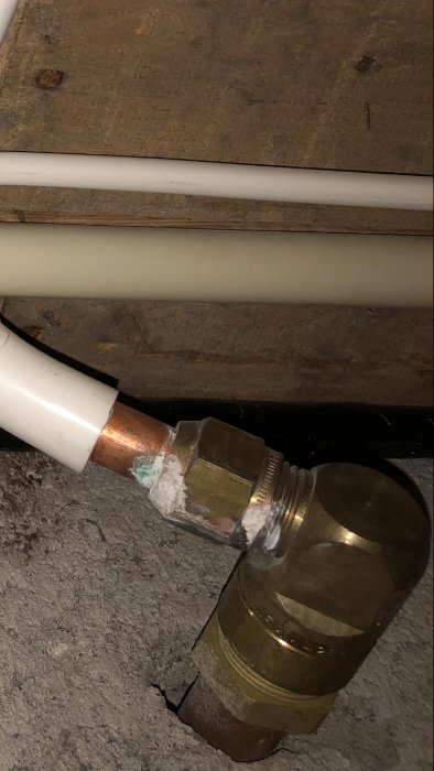 Vit vattenrör kopplad till en mässingsfärgad magnetventil med tejp, mot en träyta.