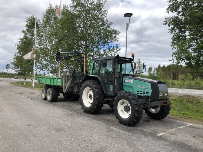 Grön traktor med timmervagn utan tippflak och med timmerstöttor, utrustad med Mowi 400-kran och vinsch.