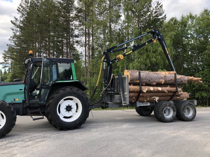 Grön traktor med lastad timmervagn utan tippflak, utrustad med Mowi 400 kran och timmerstöttor.