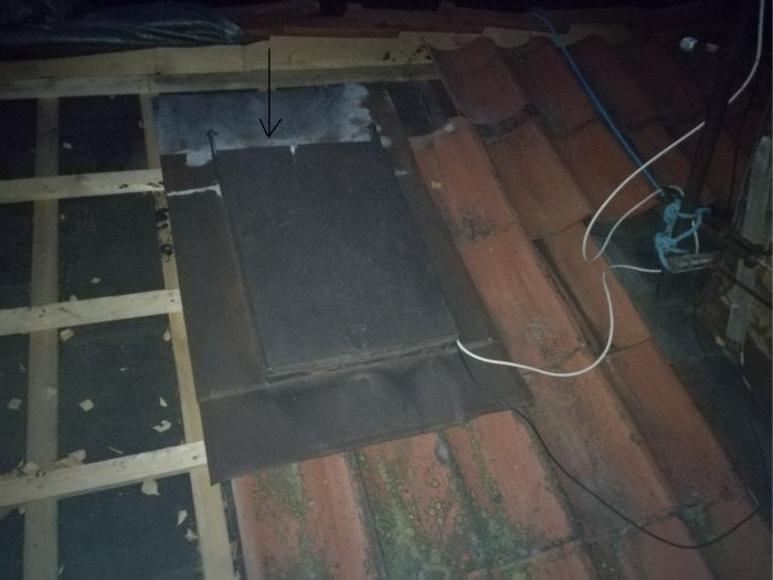 Taklucka med läckage markerat av pil, vit tätningsförsök synlig, på tegeltak vid nattetid.