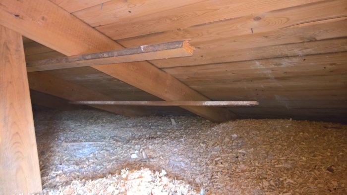 På vinden visas kutterspån på golvet med träbjälkar ovanför och en synlig ventilationslucka.