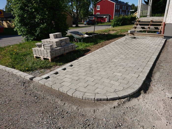Nyanlagd gångstig av gråa betongstenar med en hög oanvända stenar och en skottkärra i bakgrunden.