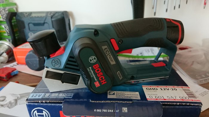 Bosch elhyvel GHO 12V-20 på förpackningen, med verktygsbatterier i bakgrunden.