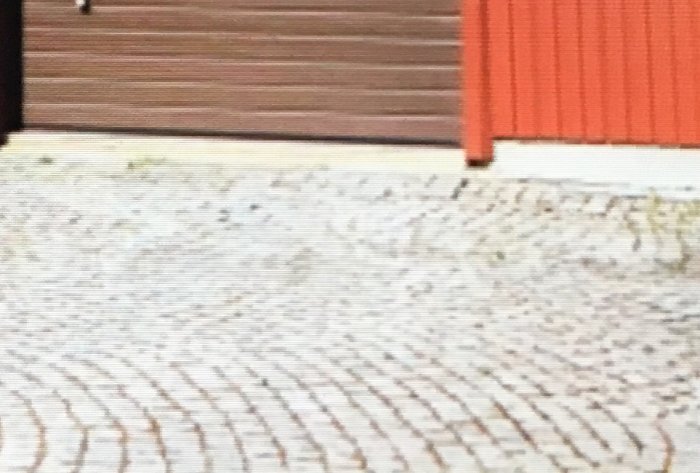 Infart med marksten beläggning framför en husfasad och garageport.