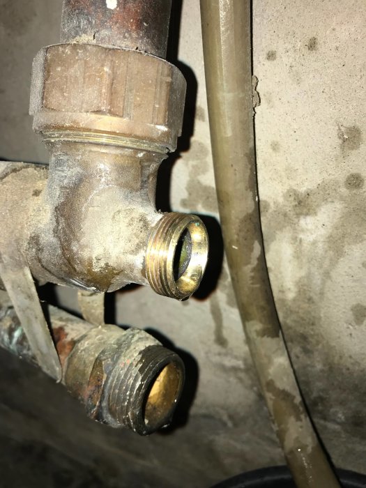 Gamla gängade rördelar i metall mot en grå betongvägg, synliga problem med att matcha nya övergångar.