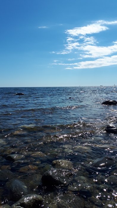 Havsvy med stenar och klart vatten vid Torö/Herrhamra, klara himmel ovanför.