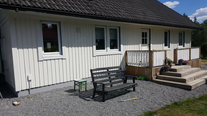 Nymålat ljusantikgrått hus med vita fönsterramar och en träveranda med blomkrukor.