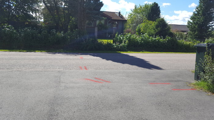 Markeringar på asfalt för potentiella elkablar vid tomt där staket ska byggas, med hus och grönska i bakgrunden.