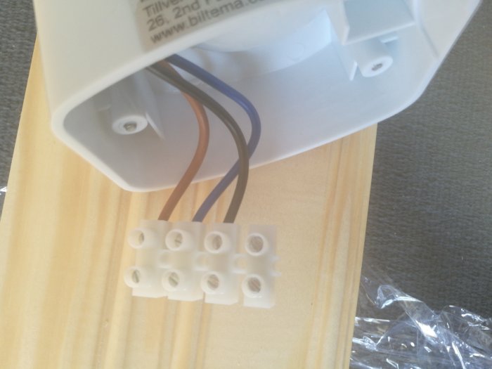 Rörelsevakt med öppet lock som visar kopplingsschema och kabelanslutningar bredvid en sockerbit.