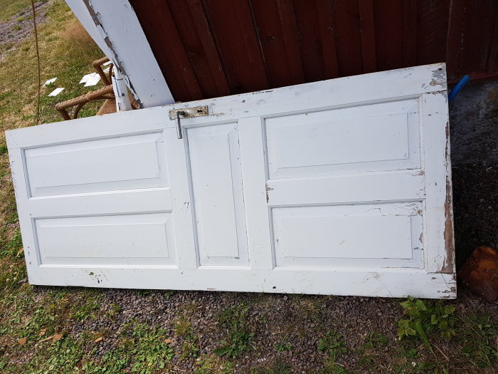 Begagnad vit spegeldörr liggande på gruset med synlig slitage och skavanker, utan karm.