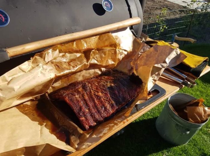 Smakrikt marinerade ribs som grillas, serverade på bakplåtspapper vid en öppen smoker-grill.