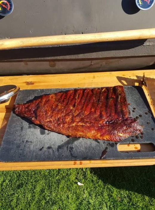 Grillade ribs på en skärbräda utomhus i solljus.