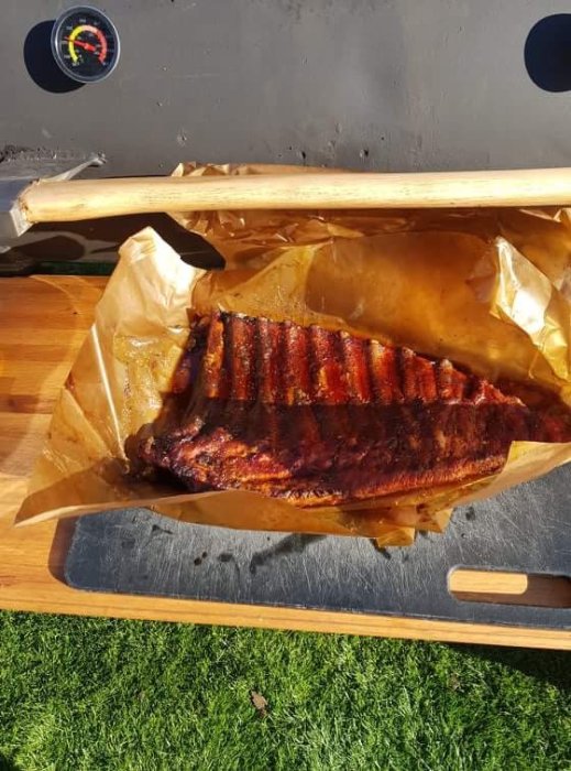 Grillade ribs på ett bakplåtspapper framför en rökgrill.