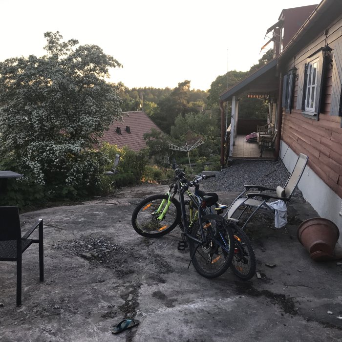 Vy över en grusad yta vid hus med cyklar, nytt fönster och rosbuske i bakgrunden.