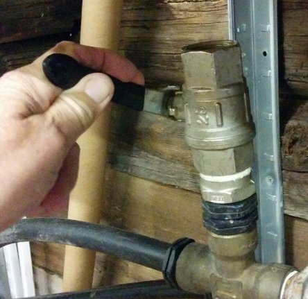 En hand fyller en sugslang med vatten genom en grov ventil på en pump, med en sil/backventil monterad.