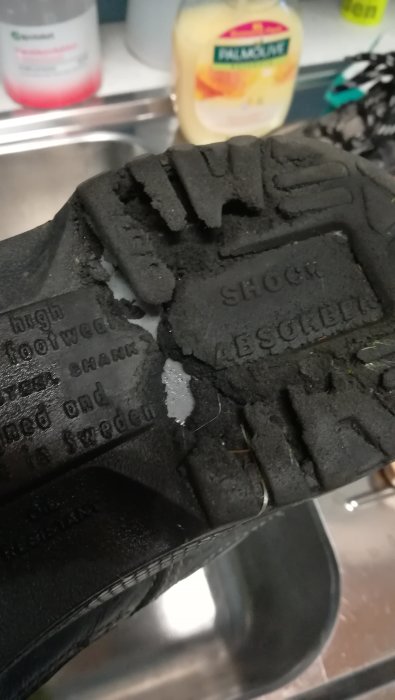 Närbild på sliten och skadad skosula med tydligt synliga skador och texten "SHOCK ABSORBING".