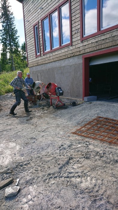 Tre personer arbetar med att gjuta källargolv med hjälp av två betongblandare utanför en byggnad.