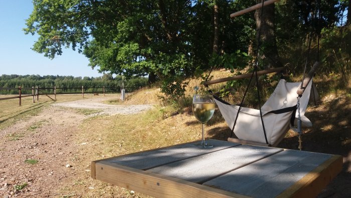 Trädgård med hängmatta, ett glas vin på bord och soligt landskap i bakgrunden.