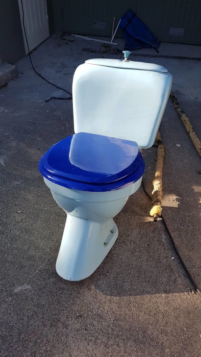 Använd toalett med blått sitslock utomhus på ett garageuppfart.