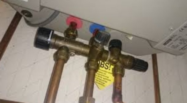 Kopplingsdetaljer under en vattenberedare med en märkt ventilkombination och färgkodade ventiler.