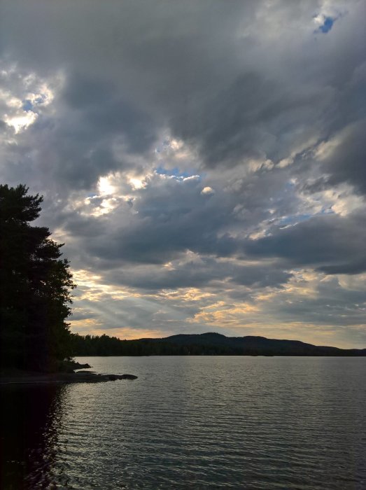 Mörka regnmoln närmar sig över en sjö med skog och berg i bakgrunden.