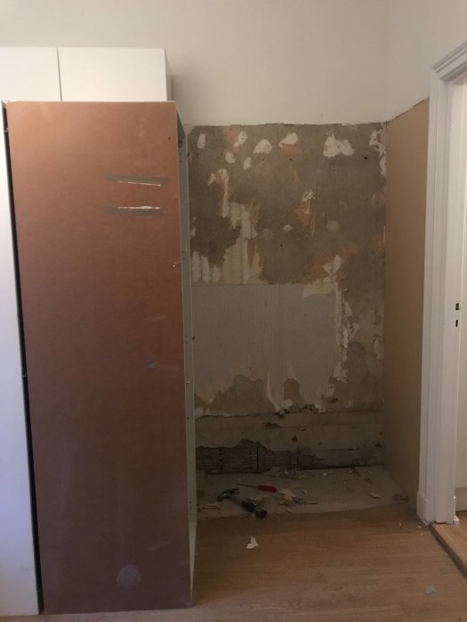 Skadad vägg där garderob tagits bort, exponerad med spikar, flagnande färg och synliga plankor.