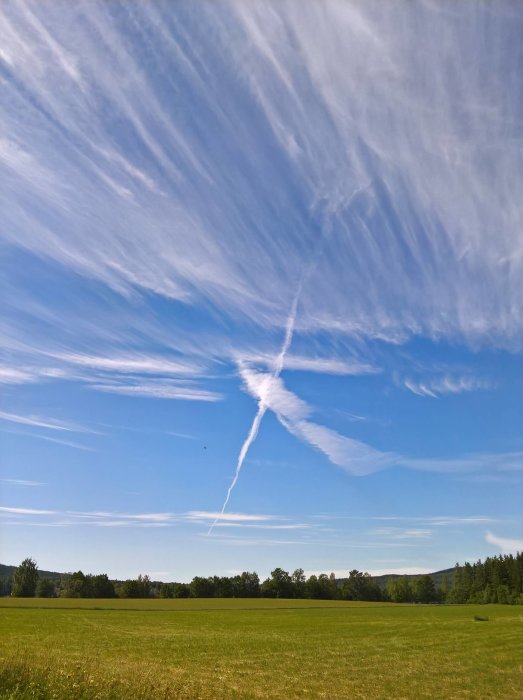 Vy över grönt fält med unika molnformationer på en klarblå himmel.