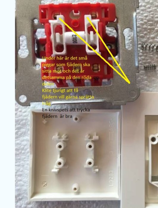 Elektrisk installationsdosa med en gul pil som pekar på små fästpunkter och antecknad text om montering.