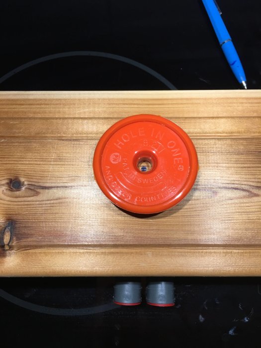 Orange magnetisk hålsökare fastsatt på träpanel ovanför två grå apparatdosor med blå elkabel.