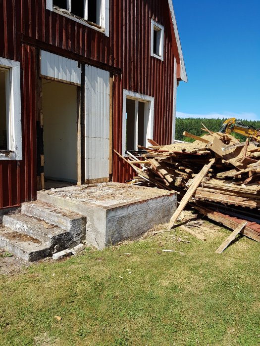 Husfasad med riven del och en hög med bråte från rivningen, synlig betonggrund och grönt gräs.