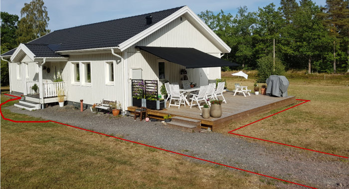 Vit husfasad med terrass och trädgård markerad för kantsten och grusläggning.