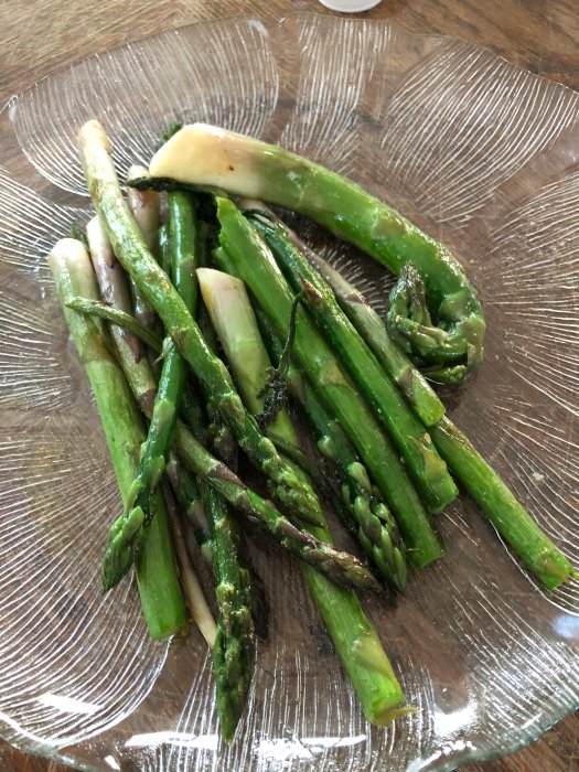 Fräsch grön sparris tillagad och serverad på ett genomskinligt fat, som en del av en hemskörd.