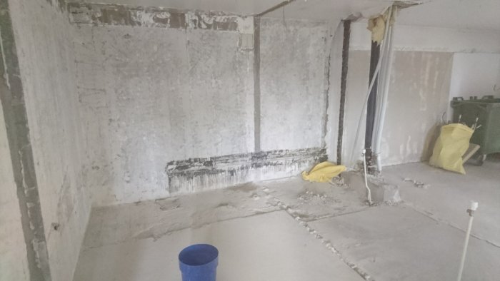 Avskalade betongväggar och golv i en ombyggnadsfas i en lägenhet, med synliga rör och kablar.