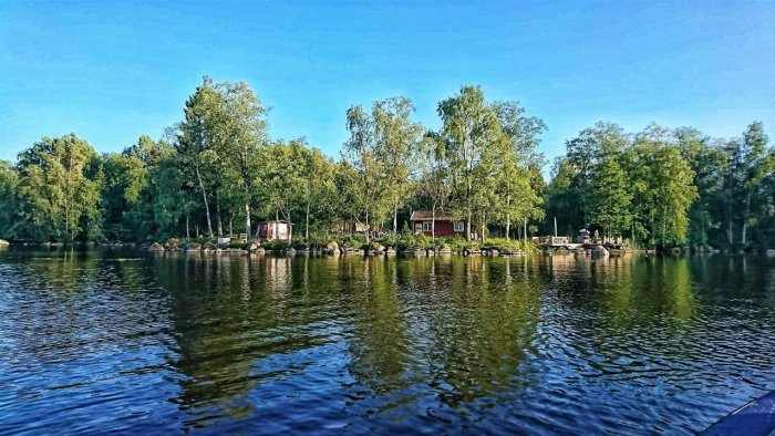 Idylliskt hus omgivet av träd vid Krokviks vattenkant under blå himmel.