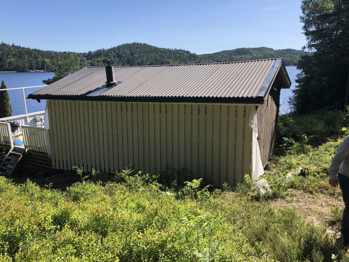 Hus med ny fasad och fönster, vid sjö med skog i bakgrunden.