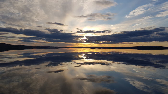 Solnedgång med spegelblank sjö och moln i Jämtland, fotograferad från en utterbräda.