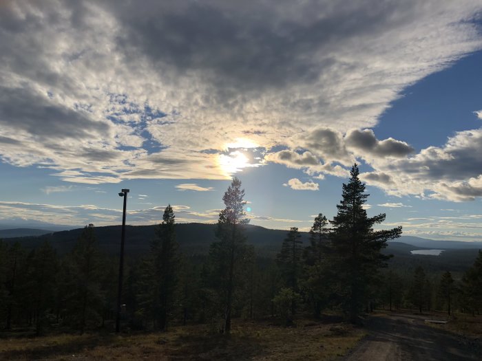 Solnedgång över skogsbeklädd bergsterräng med molnig himmel.