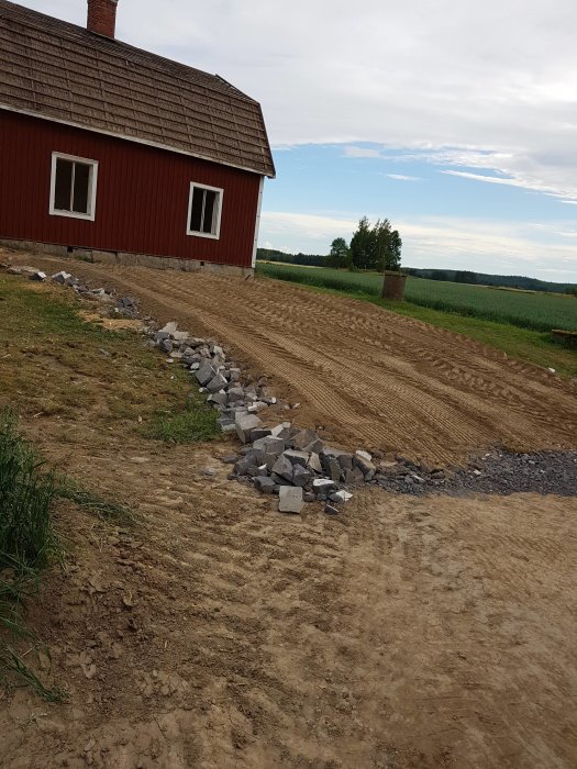 Nyplanerad mark med kantstenar bredvid rött hus efter garage rivning.