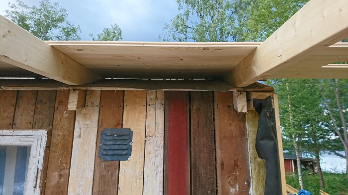 Nyinstallerade träbjälkar på en veranda under konstruktion, med en för kort bjälke nära husets vägg.