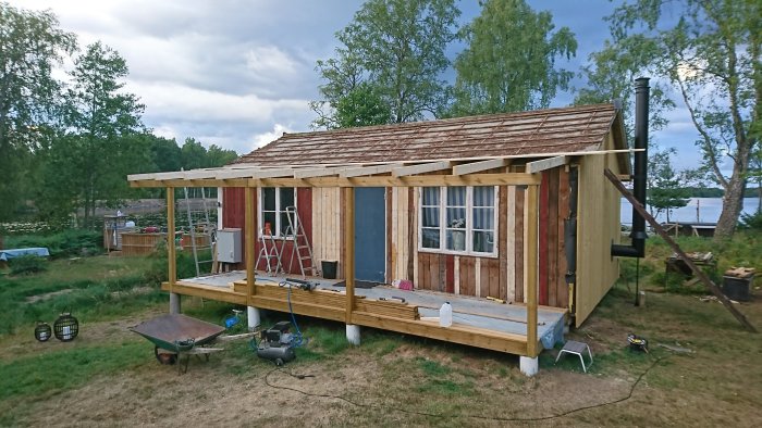 Renoveringsprojekt av veranda med nya takbjälkar och verktyg på verandan, natur och sjö i bakgrunden.