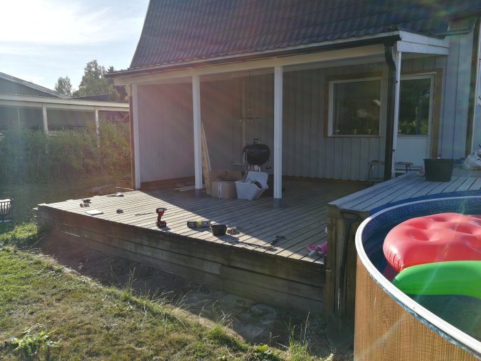 Altan under ombyggnad med verktyg utspridda, delvis under tak nära huset och en uppsätt bassäng till höger.