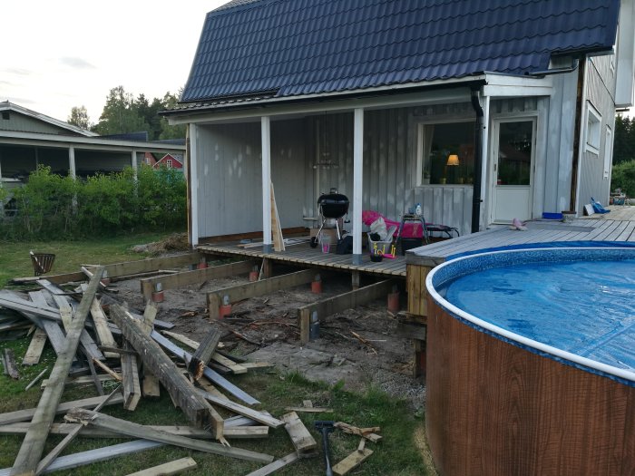Altan under renovering med träplankor på marken, oavslutad konstruktion och en intilliggande pool.